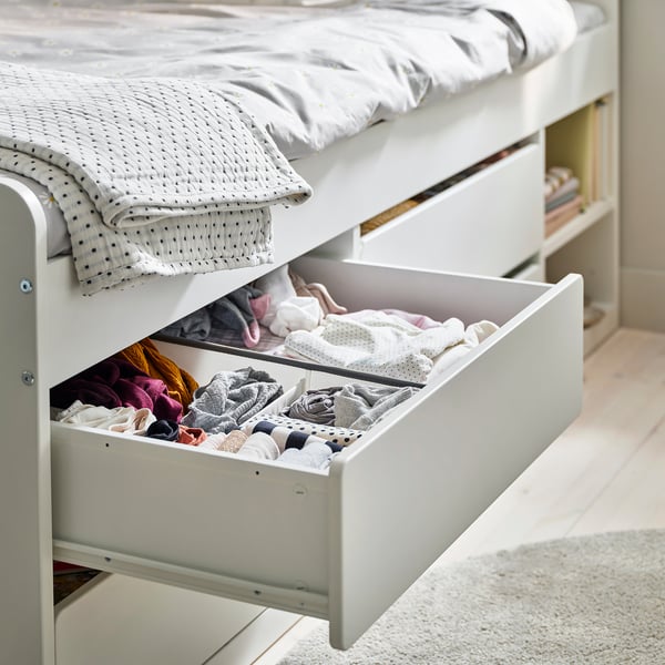 Open white bed drawer showing folded clothes, demonstrating storage space. Bed has drawers underneath for ample storage.
