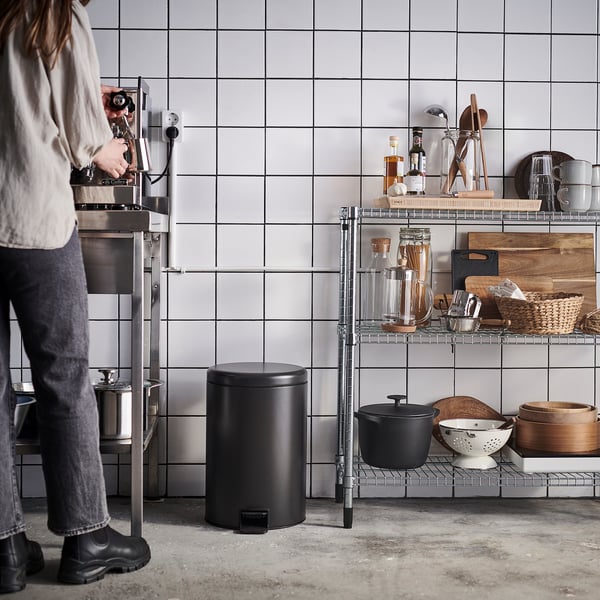 Person operating a coffee machine in a modern kitchen with black bins and shelves holding various kitchen items.