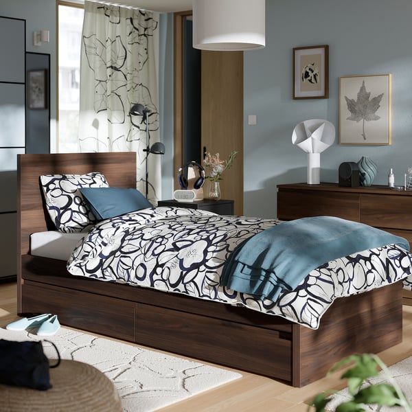 Modern bedroom with STORKLINTA bed; patterned blue bedding, wood frame, two under-bed drawers. Tall headboard, matching decor.