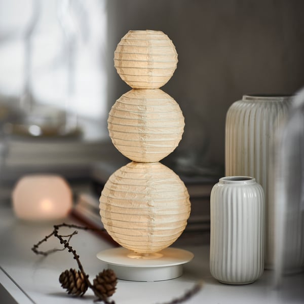 Beige STRÅLA lamp, soft round shape, between vase and sphere, table with pinecone & branches.