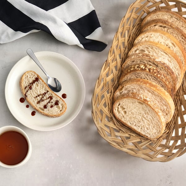 Wicker bread basket with sliced bread, cloth, and jam. Natural, warm, and inviting.