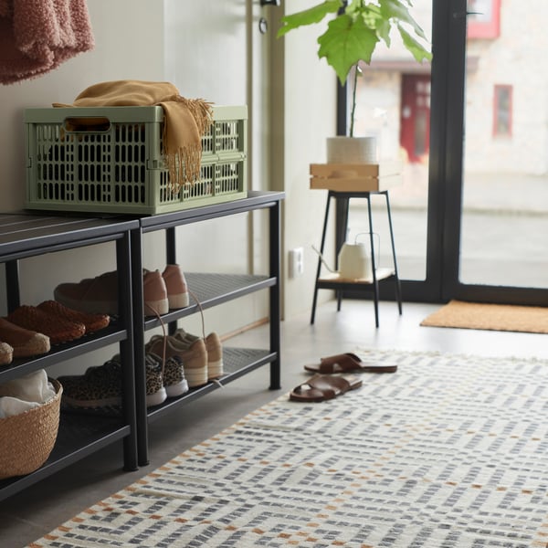 Entryway with green VEDKLYV box on shoe rack, near plant and door.