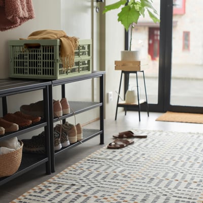 Entryway with green VEDKLYV box on shoe rack, near plant and door.