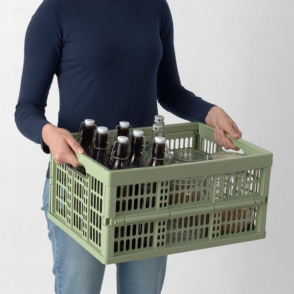 Person carrying a green plastic crate filled with bottles.