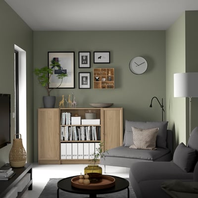 Grünes Wohnzimmer mit grauem Sofa, BILLY Bücherregal, Uhr und Couchtisch.