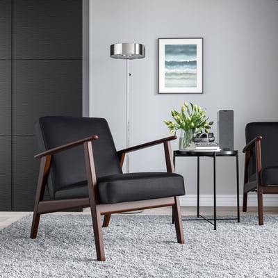 Minimalistisches Wohnzimmer mit 2 schwarzen EKENÄSET-Stühlen, Beistelltisch, Blumen, Büchern und Wandkunst.
