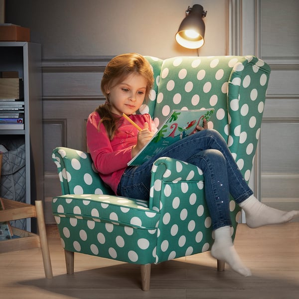 Mädchen im türkisfarbenen Polka Dot Stuhl liest Buch.