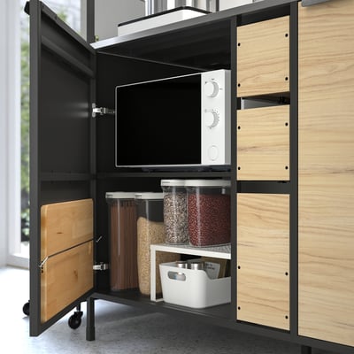 Organised kitchen cabinet with microwave, containers, and cutting board.