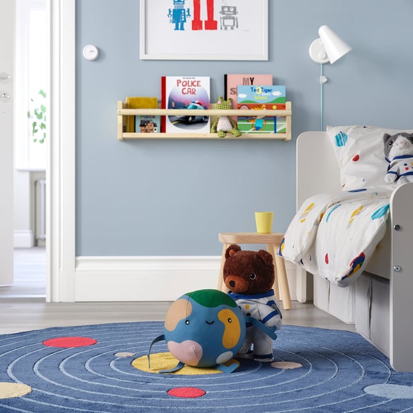 Kids room with toddler bed, blue rug, astronaut plush, and books.