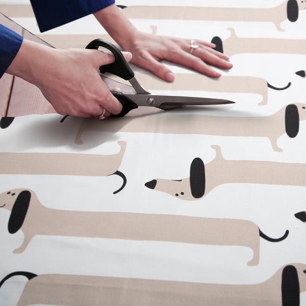 Person cuts fabric with scissors. Pattern shows cartoon dogs.