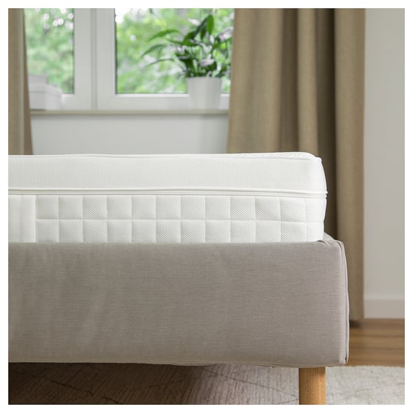 A white ÅVABERG foam mattress with a textured cover, placed near a window.