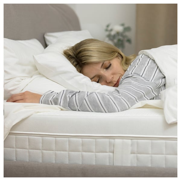 A person sleeps peacefully on a white ÅVABERG mattress, covered with clean linens in a serene bedroom.