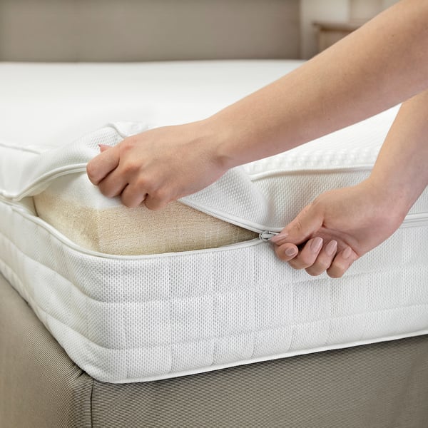 A person zips a white mattress protector onto a foam mattress, showcasing easy installation for cleanliness and comfort.