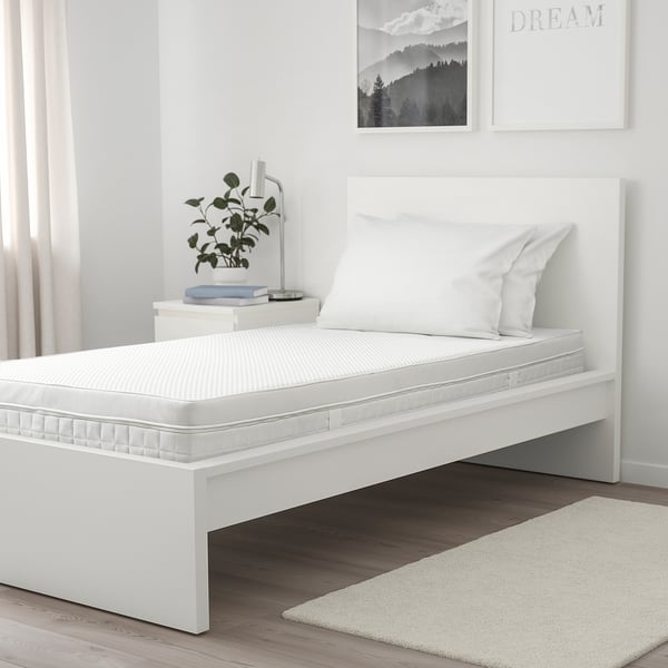 Minimalist bedroom with ÅVABERG bed, art, lamp, plant, books, and rug.