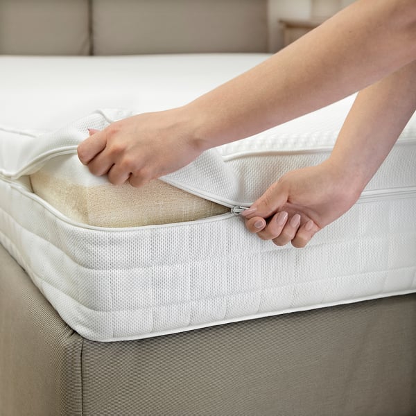 Person zips white mattress protector on bed.