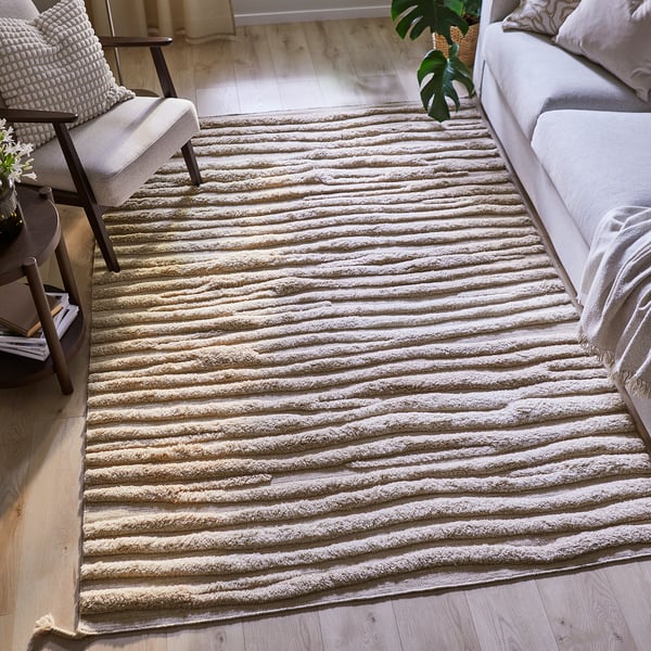 A light grey, striped, hand-woven wool rug in a living room with a couch and chair.