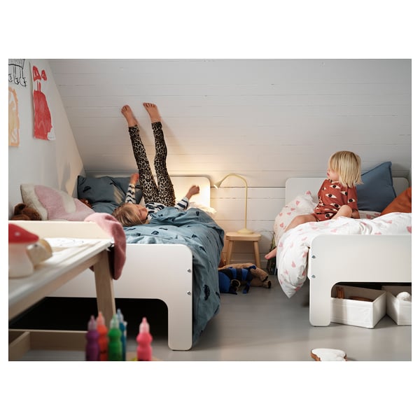 Kids bedroom with white bunk beds, one child sleeps while another reads, colorful crayons on the floor.