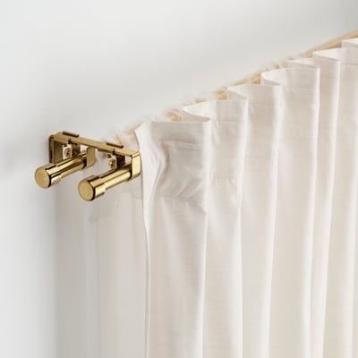 White curtains hang from a gold BEKRÄFTA rod set, including wall brackets and holders, attached to a white wall.