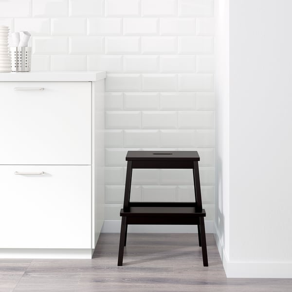 Black step stool next to white cabinet, ideal for reaching high items.