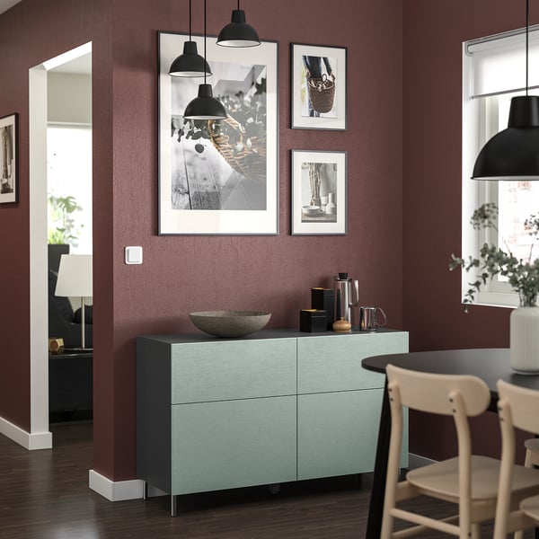 Modern room with maroon walls, a turquoise BESTÅ storage unit, wooden chairs, and black pendant lights, framed art hanging above.