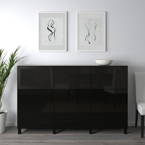Black glossy sideboard with two white framed artworks above, a white bowl on top, and a potted plant on the left.