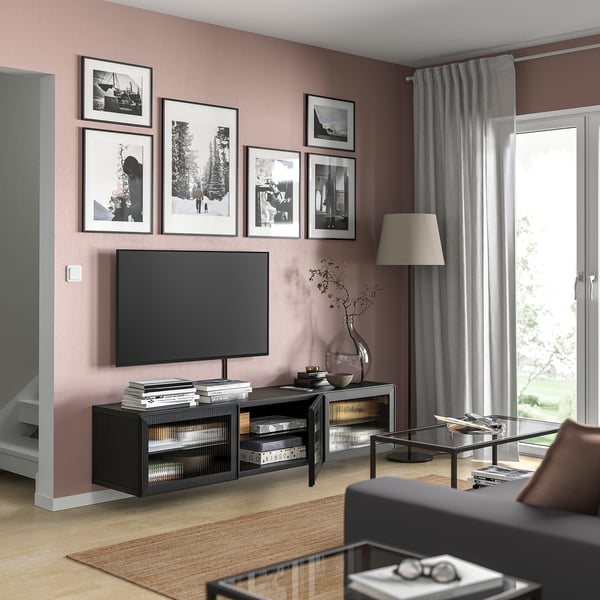 Living room with tv on modern black BESTÅ stand, pink walls, grey curtains, framed photos, lamp, and glass coffee table.