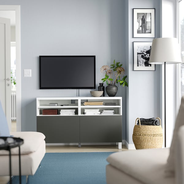 Modern living room with BESTÅ tv bench in white and black, featuring a flat-screen tv, decorative items, and a blue rug.