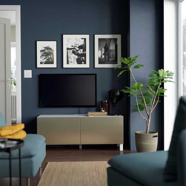 Modern living room with dark walls, light green BESTÅ tv bench, tv, decor, blue seats, plant, and black-and-white art.