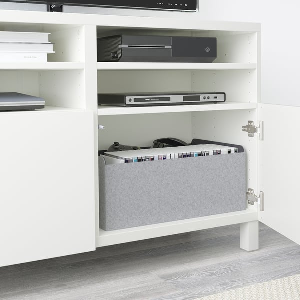 White BESTÅ tv bench with adjustable shelves, storing gaming console, remotes, and dvd player. Hidden cables, soft-close doors, rear cable outlets.