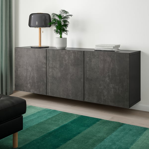 Dark grey floating sideboard under a lamp; plant & books on top, green rug below; chair to left.