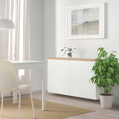 Modern BESTÅ storage unit with single cabinet, wood top, beach art, plants, and desk.