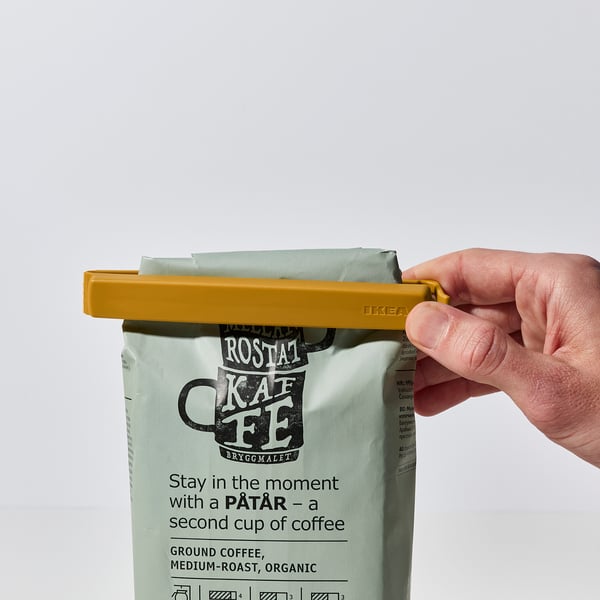 Hand closes yellow clip on coffee bag, sealing it, ensuring freshness.