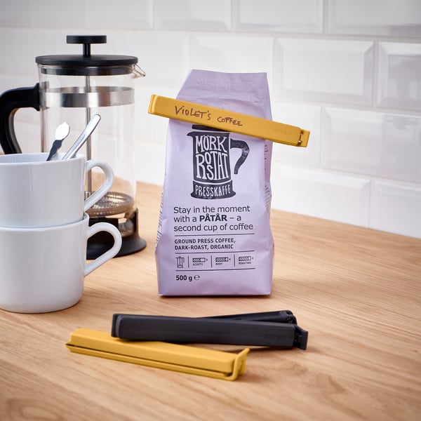 Sealed coffee bag with clips on a counter. Includes cafetière and mugs.