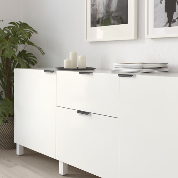 White cabinet with black handles, decorative candles, stacked books, and plant beside it.