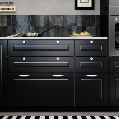 Modern black kitchen with BODBYN drawer fronts, round knobs, and white marble countertop. Dark cabinets and stainless steel appliances.