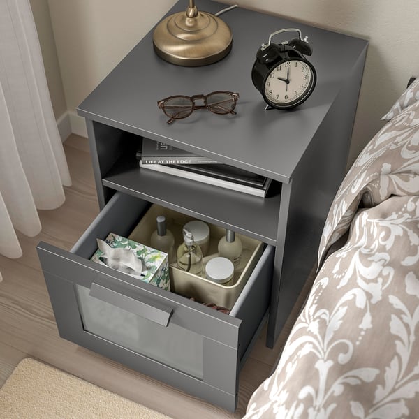 Modern bedside table with power outlet, drawer for storage, and decorative items on top.