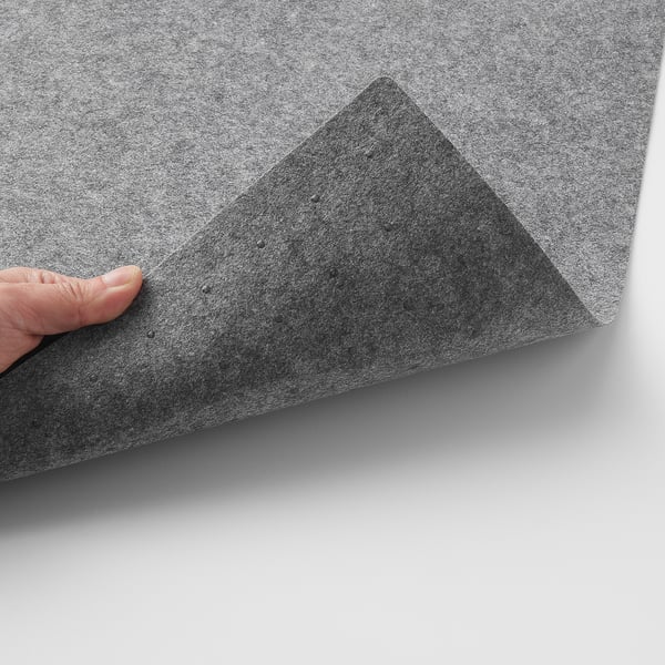 Hand holding grey table mat with textured surface and small silicone dots underneath, shown from the corner.