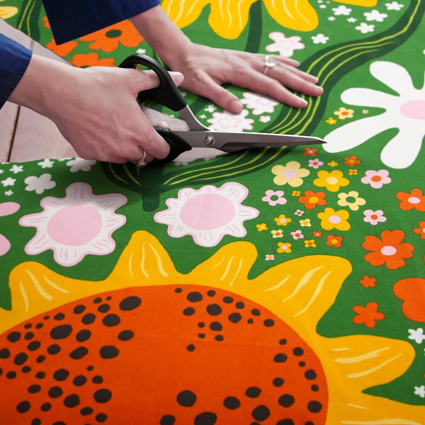 Cutting sunflower-patterned fabric with scissors for sewing projects.