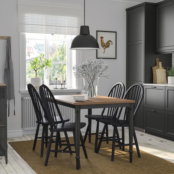 Modern dining set with black legs, wood top, seats four, large light, small window, grey cabinets.