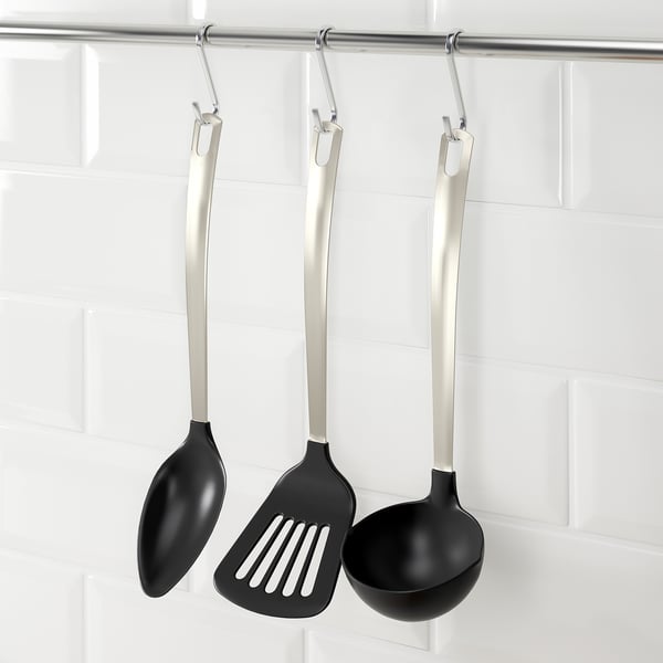 Three black cooking utensils with silver handles hang from hooks: spoon, spatula, and ladle, designed for non-stick pots and pans.
