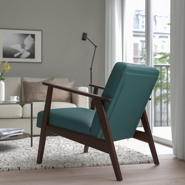 Teal upholstered retro-style armchair with wooden legs sits by a window in a cosy living room.