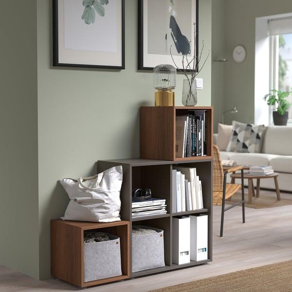 Wooden EKET cube shelves in honey shade with books and decor against green wall.