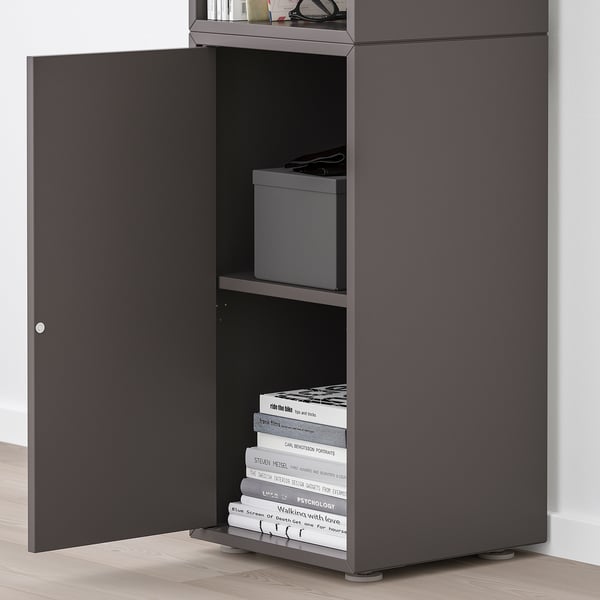 Black EKET cabinet with one door open, revealing shelves holding books and storage boxes.