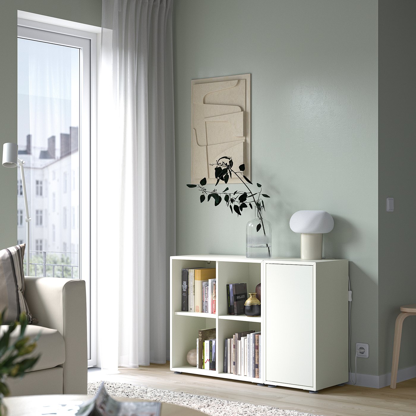 Small white EKET cube shelves under a window, holding books and decor. Light blue wall with abstract art.