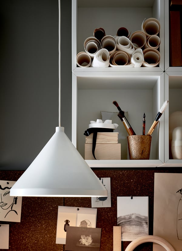 Modern white pendant lamp hangs near organised shelves with art supplies in white cabinet, blue wall.