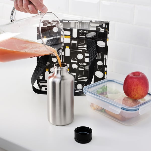 Hand pours drink into silver insulated bottle beside packed lunch.