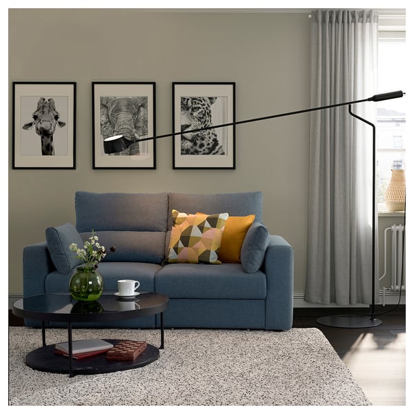 Modern living room with grey ebkilstuna sofa, colourful pillows, black coffee table, art prints on wall, curtains, and floor lamp.