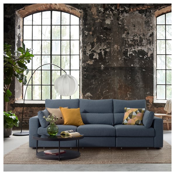 Modern living room with blue ESKILSTUNA sofa, colourful pillows, round coffee table, large arched windows, and floor lamp.