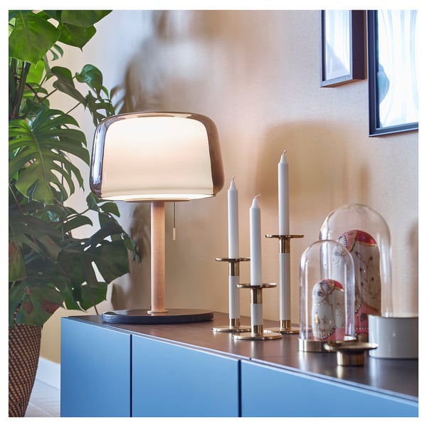 Stylish modern lamp, gold colour, glass and brass. On blue cabinet, plants and decor nearby.