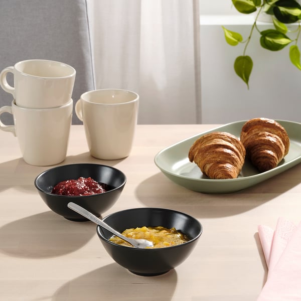 Table set with FÄRGKLAR bowls and mugs, containing jam and yoghurt, ready for breakfast.